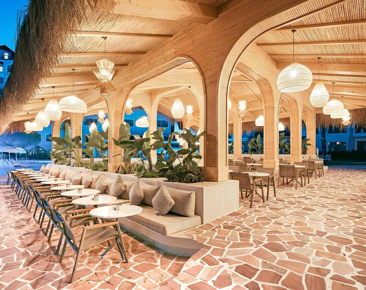 Luxury resort restaurant featuring natural stone flooring with organic irregular patterns, warm ambient lighting, tropical modern architecture, elegant outdoor dining seating, textured stone surface, and premium hospitality interior design inspiration.