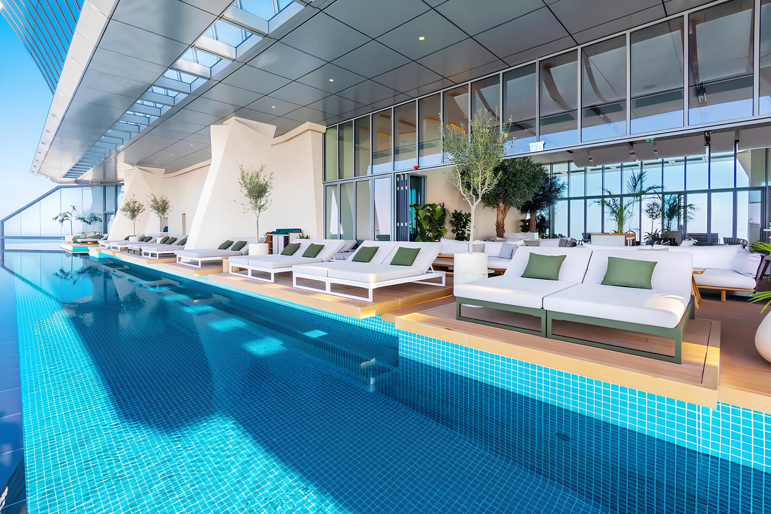 Luxury indoor swimming pool with cyan glass mosaic tiles, modern resort design, poolside lounge seating, and premium spa environment by Roman Mosaic, leading pool tile supplier UAE.