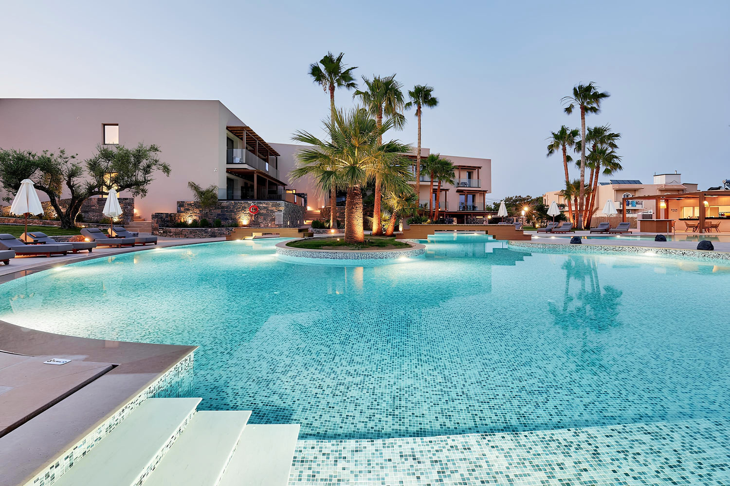 Luxury resort swimming pool with blue glass mosaic tiles, crystal-clear water, modern villa surroundings, and premium pool design by Roman Mosaic, leading swimming pool tile supplier UAE.